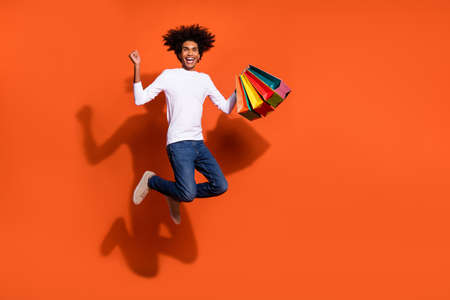 Photo of amazed lucky guy wear white shirt jumping high rising bargains empty space isolated orange...