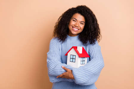 Photo of young cheerful girl hug cuddle house relocation property isolated over beige color backgroundの写真素材