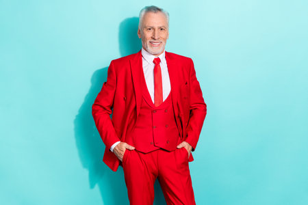 Portrait of attractive cheery chic grey-haired man holding hands in pockets isolated over bright teal turquoise color backgroundの写真素材