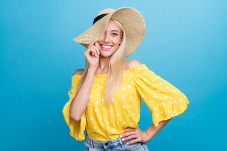 Photo of cute young blong lady hand hat wear yellow top cap isolated on blue color backgroundの写真素材
