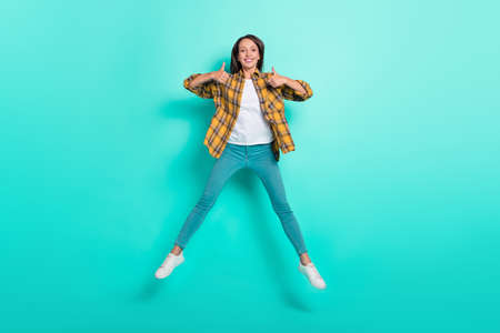 Full size photo of young cool brunette lady jump show thumb up wear shirt jeans shoes isolated on turquoise backgroundの写真素材