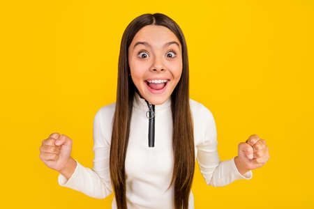 Photo of impressed lucky preteen girl dressed white zipper shirt rising fists smiling isolated...