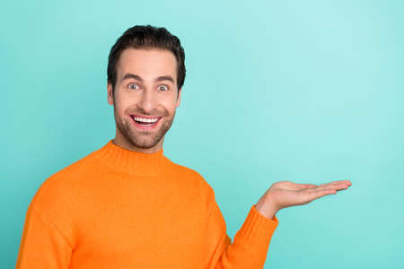 Portrait of astonished man hand palm demonstrate hold empty space proposition isolated on teal color backgroundの写真素材