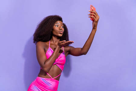 Photo of sweet flirty african lady dressed pink sexy clothes sending kiss recording video modern device isolated violet color backgroundの写真素材