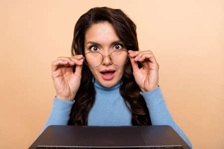 Photo of shiny impressed woman wear sweater arms spectacles looking modern gadget isolated beige...