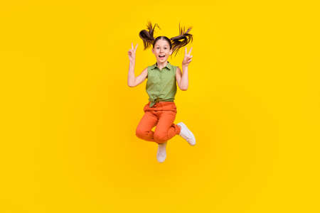 Photo of cute charming preteen girl dressed green top showing two v-signs jumping high smiling...