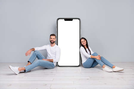 Photo of pretty lady guy wear shirts sit floor near cellphone poster isolated concrete grey wall...