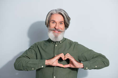 Portrait of attractive cheery trendy grey-haired man showing heart sign care isolated over gray...