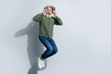 Photo of impressed man pensioner dressed khaki shirt arms hands spectacles jumping high isolated grey color backgroundの写真素材