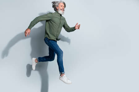 Photo of handsome man pensioner dressed khaki shirt running empty space jumping high isolated grey...