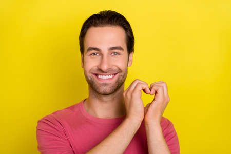 Photo of affectionate guy arms presenting heart shape sign wear pink t-shirt isolated yellow color backgroundの写真素材