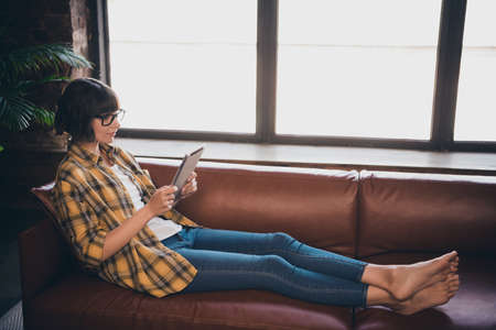 Photo of pretty sweet lady dressed plaid shirt glasses relaxing couch reading modern device indoors workstation workshopの写真素材