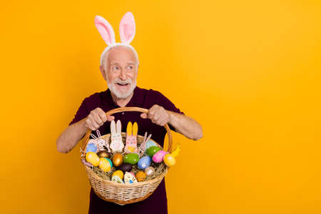 Photo of cheerful mature man hold wicker basket colorful cookies look empty space isolated over yellow color backgroundの写真素材