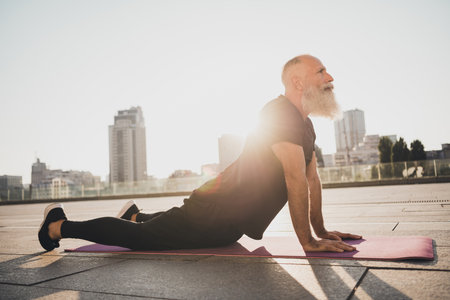 Photo of focused concentrated old trainer man lay mat carpet do cobra pose wear t-shirt urban town...