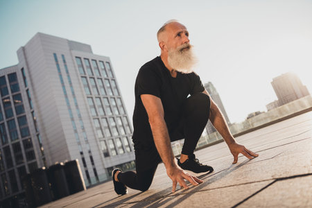 Photo of cool retired motivated old man stand ready position prepare run marathon wear t-shirt urban town outsideの写真素材