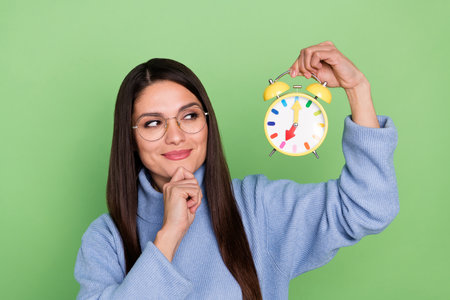 Photo of thinking young brunette lady look clock wear blue pullover eyewear isolated on green color...