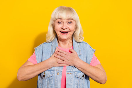 Photo of impressed funny retired woman wear jeans vest arms chest open mouth isolated yellow color...