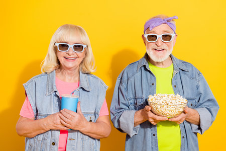 Photo of funny cute husband wife wear jeans shirts watching movie eating popcorn isolated yellow color backgroundの写真素材