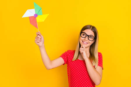 Photo of youth lovely girl have fun hand touch chin hold origami eyewear isolated over yellow color backgroundの写真素材