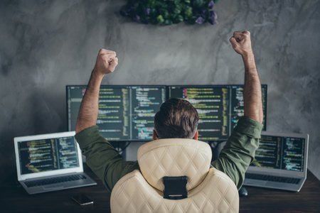 Photo of lucky astonished young man wear green shirt spectacles winning online trade rising fists indoors workshop workstationの写真素材