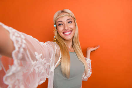 Self-portrait of attractive cheerful girl demonstrating copy space isolated over bright orange color...