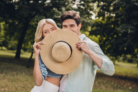 Portrait of two attractive funny flirty coquettish couple having fun romance hiding face behind cap...