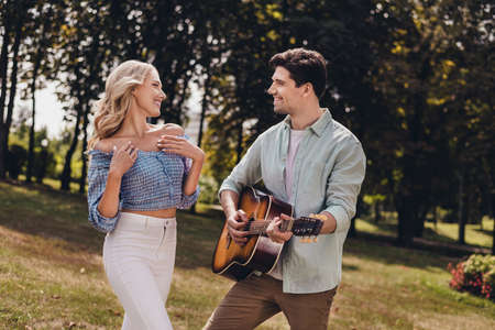 Portrait of two attractive cheerful couple guy playing guitar spending holiday having fun outdoors