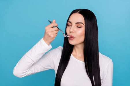 Photo of young nice brunette lady hold spoon eat wear white cloth isolated on blue color background