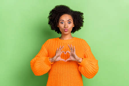 Photo of coquette young wavy hairdo lady show heart blow kiss wear orange jumper isolated on green color backgroundの写真素材