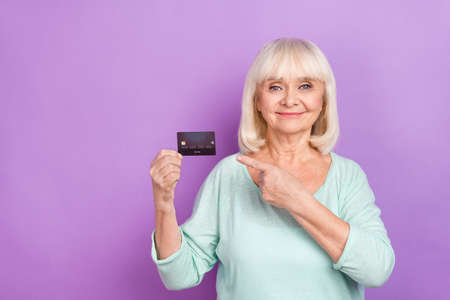 Photo of nice positive old lady direct forefinger debit card wear turquoise shirt isolated violet...