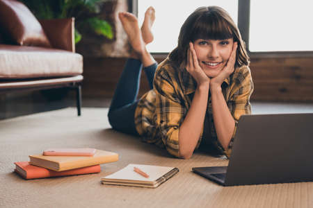 Photo of charming lovely relaxing college student female lying floor preparing homework in laptop in...
