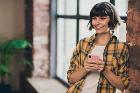 Photo of nice young bob hairdo lady hold telephone wear yellow shirt at loft home in flat aloneの写真素材