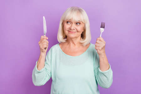 Photo of positive curious hungry lady hold knife fork look empty space wear teal shirt isolated violet color backgroundの写真素材