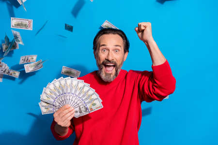 Portrait of attractive cheerful man holding cash flying credit loan rejoicing isolated over bright blue color backgroundの写真素材