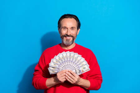 Portrait of attractive cheerful man holding in hands fan cash atm isolated over bright blue color backgroundの写真素材