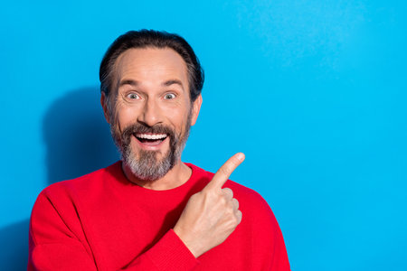 Photo of cheerful laughing amazed guy advertising product suggest pick object isolated on blue color backgroundの写真素材