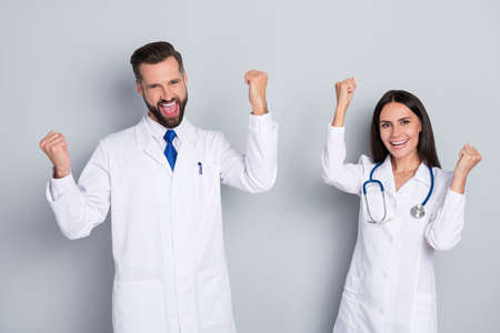 Portrait of two attractive cheerful lucky medics rejoicing having fun practicing isolated over grey...