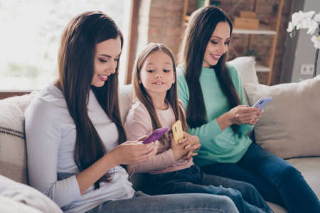 Profile side photo of cheerful ladies use cellphone chatting typing sms fast connection 4g sit divan indoorsの写真素材