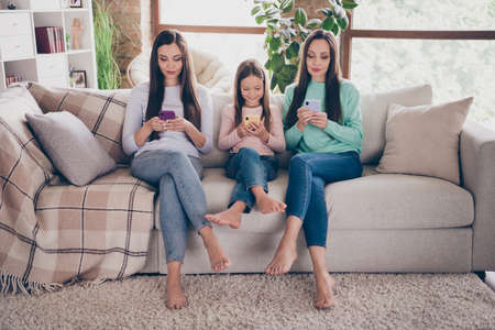 Full length photo of mommy siblings rest free-time use mobile childhood comfort post repost social network barefoot indoorsの写真素材