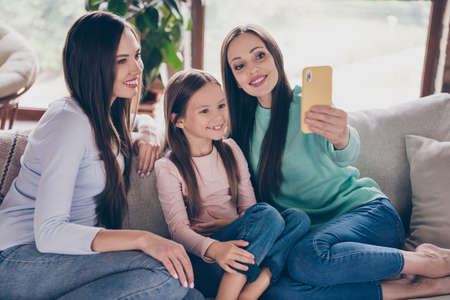 Photo of three charming girl shoot selfie picture speak video call cellphone sitting divan flat...