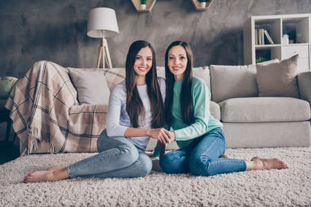Portrait of two attractive cheerful people friends family sitting on floor cuddling spending time at home indoorsの写真素材