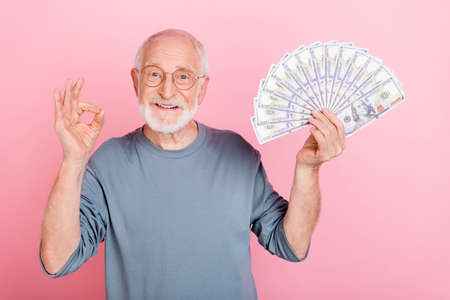 Photo of cheerful cute retired man grey sweater spectacles rising cash fan okey sign isolated pink color backgroundの写真素材