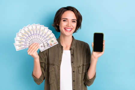 Photo of cool young short hairstyle lady show money telephone wear khaki shirt isolated on blue...
