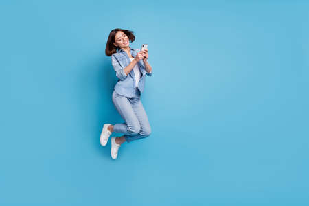 Photo of pretty sweet lady dressed denim shirt jumping typing gadget empty space isolated blue color backgroundの写真素材