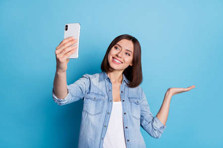 Photo of shiny cute lady dressed denim shirt tacking selfie gadget arm empty space isolated blue...