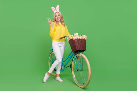 Photo of funny cute lady dressed yellow pullover headband driving cycle showing v-sign isolated green color backgroundの写真素材