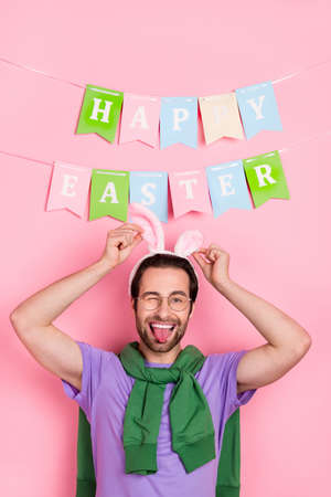 Photo of funny good mood male fooling around showing tongue celebrate easter isolated on pink color backgroundの写真素材