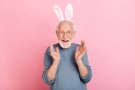 Photo of impressed funny retired man grey sweater spectacles bunny ears rising arms isolated pink color backgroundの写真素材