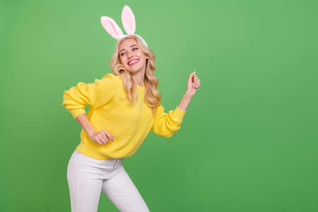 Photo of funky young blond lady dance look promo wear ears yellow pullover pants isolated on green color backgroundの写真素材