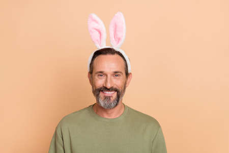 Portrait of attractive funny cheerful man wearing festal fluffy accessory isolated over beige pastel color backgroundの写真素材